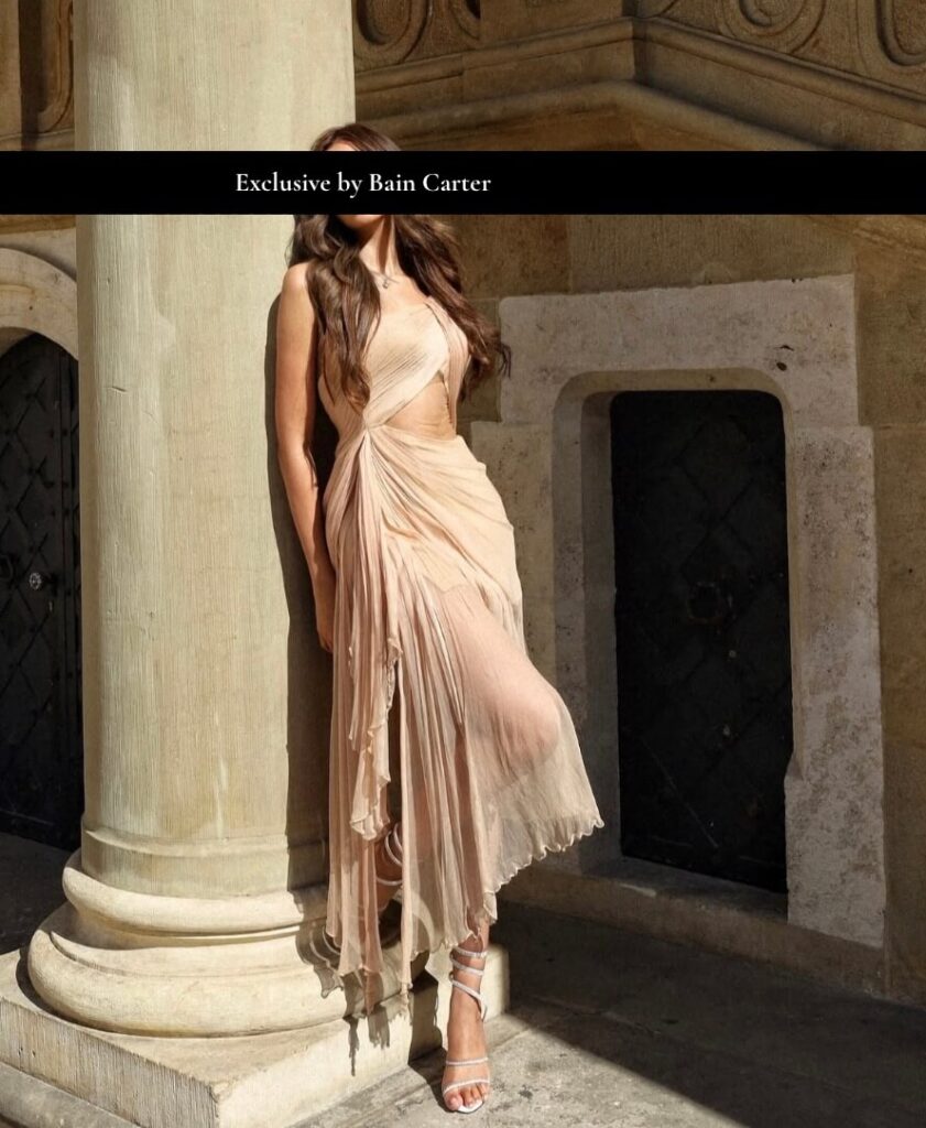 Elegant luxury escort wearing golden dress beside classical columns with refined vip companion style