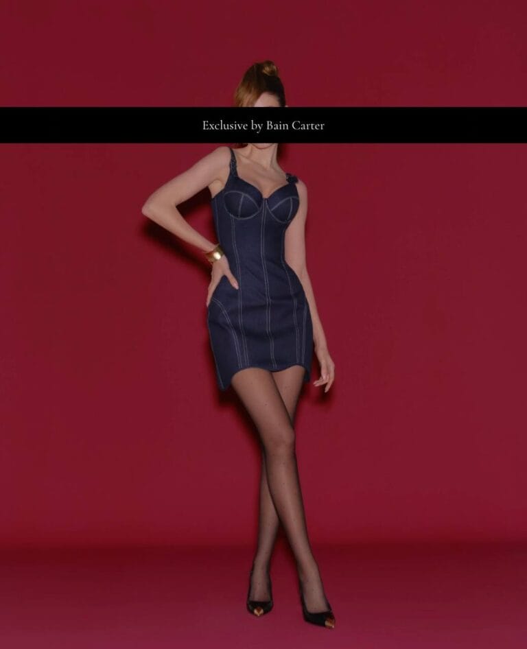 Karolina posing in a short navy dress and black tights against a burgundy background