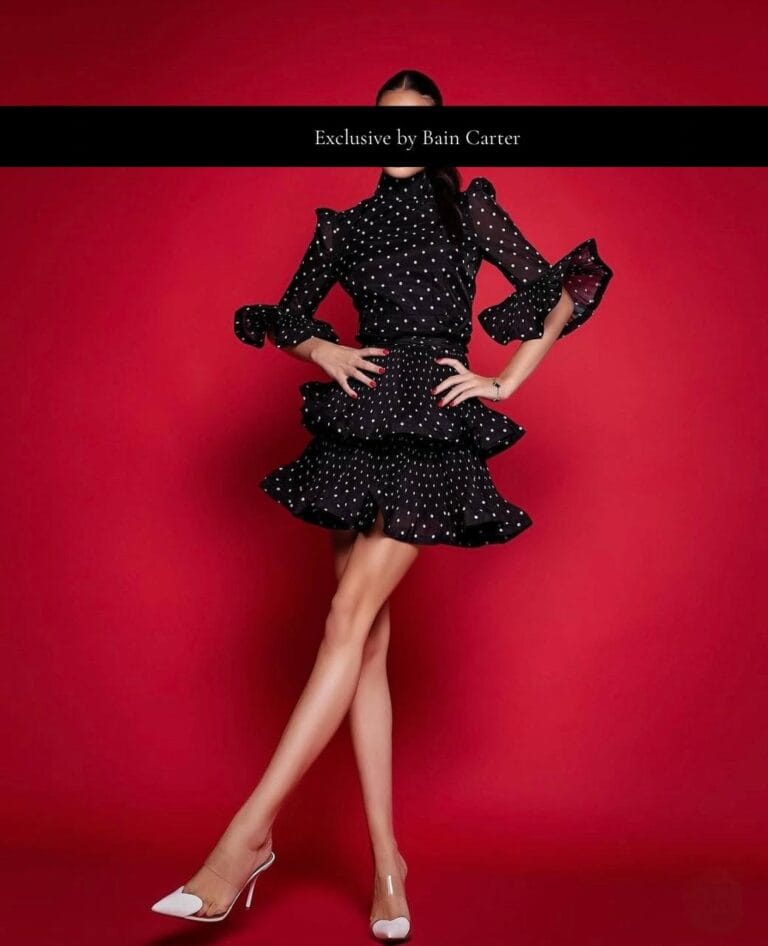 Teodora wearing a black ruffled dress and white heels against a red background