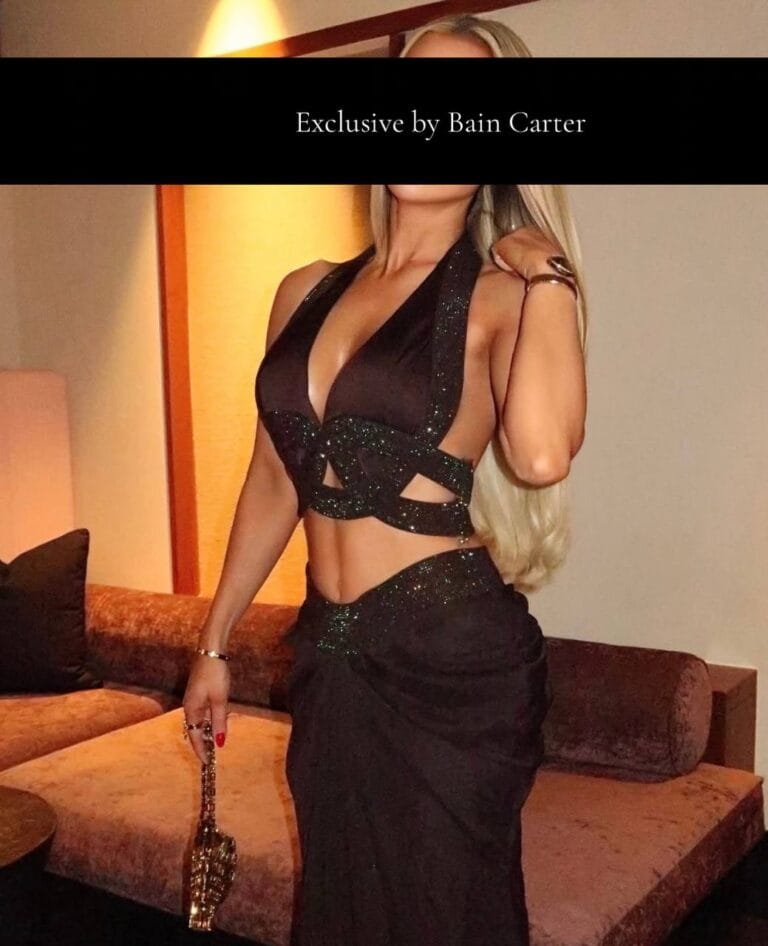 Lauren wearing a sparkly black crop top and matching long skirt standing near a velvet sofa.
