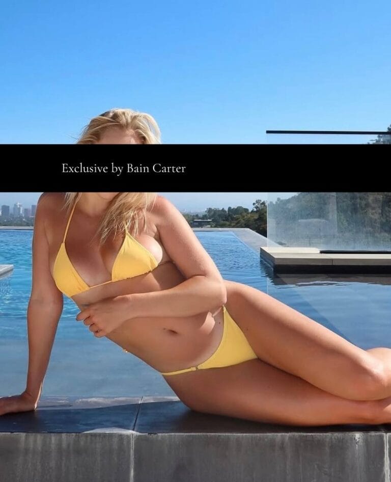 Madison wearing a yellow bikini posing by an infinity pool with hills in the background.