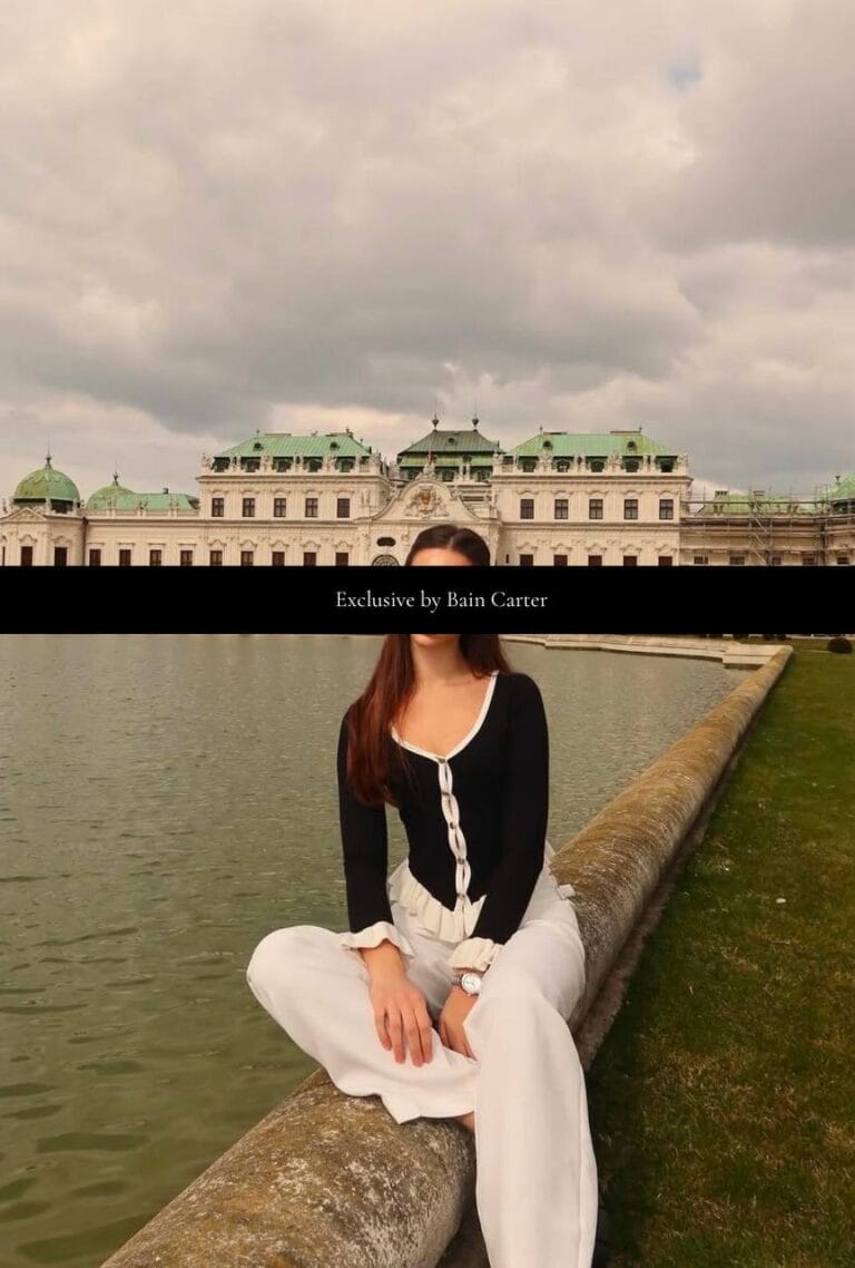 Woman sitting beside the water wearing a black top and white trousers